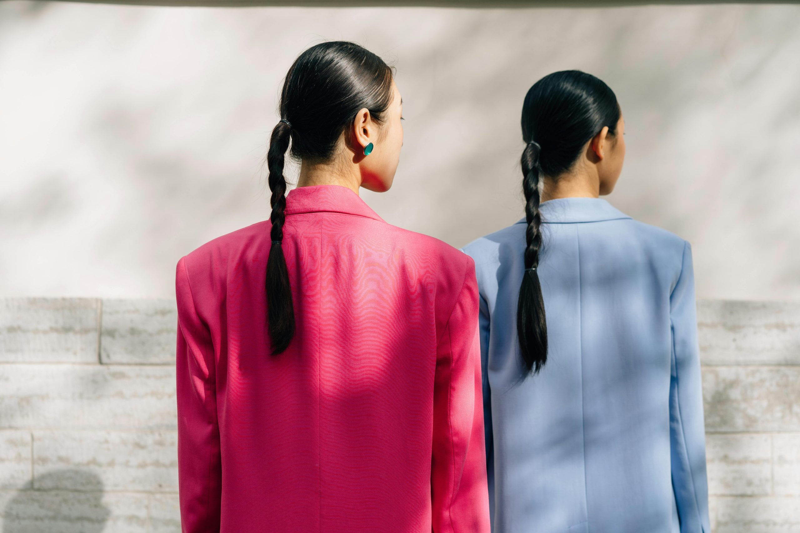 Two women in bright blazers facing a textured wall.