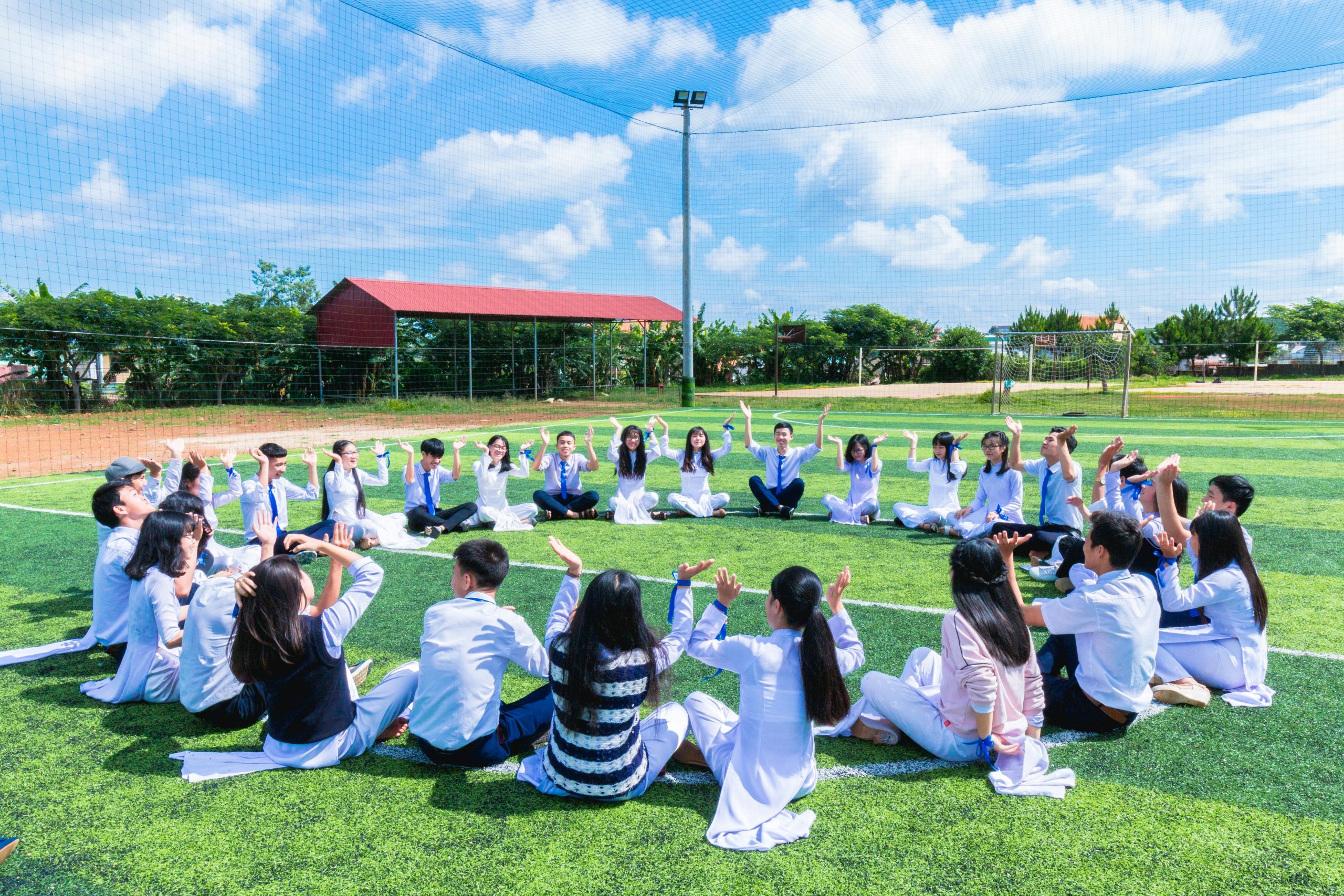 Students seated in a circle on a school field engaging in outdoor activities.