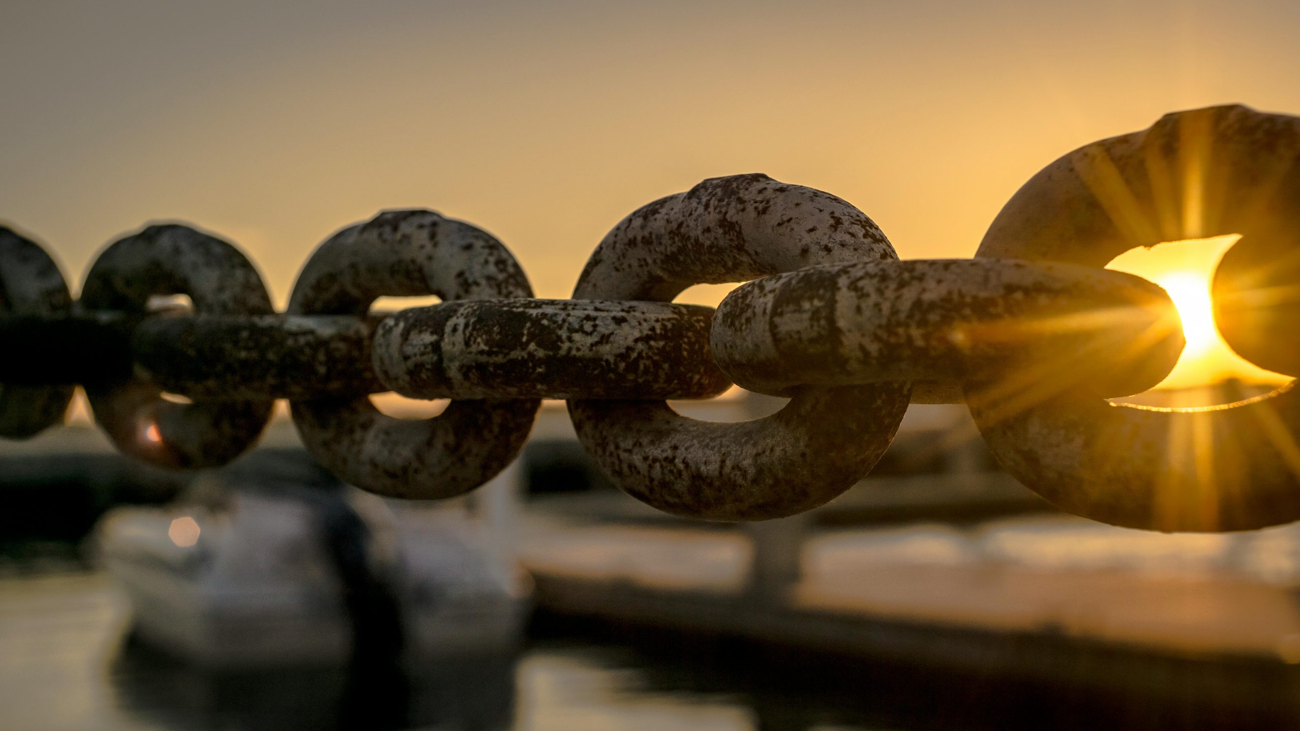 Close-up of a rusty chain with sunrise and water reflections in the background.