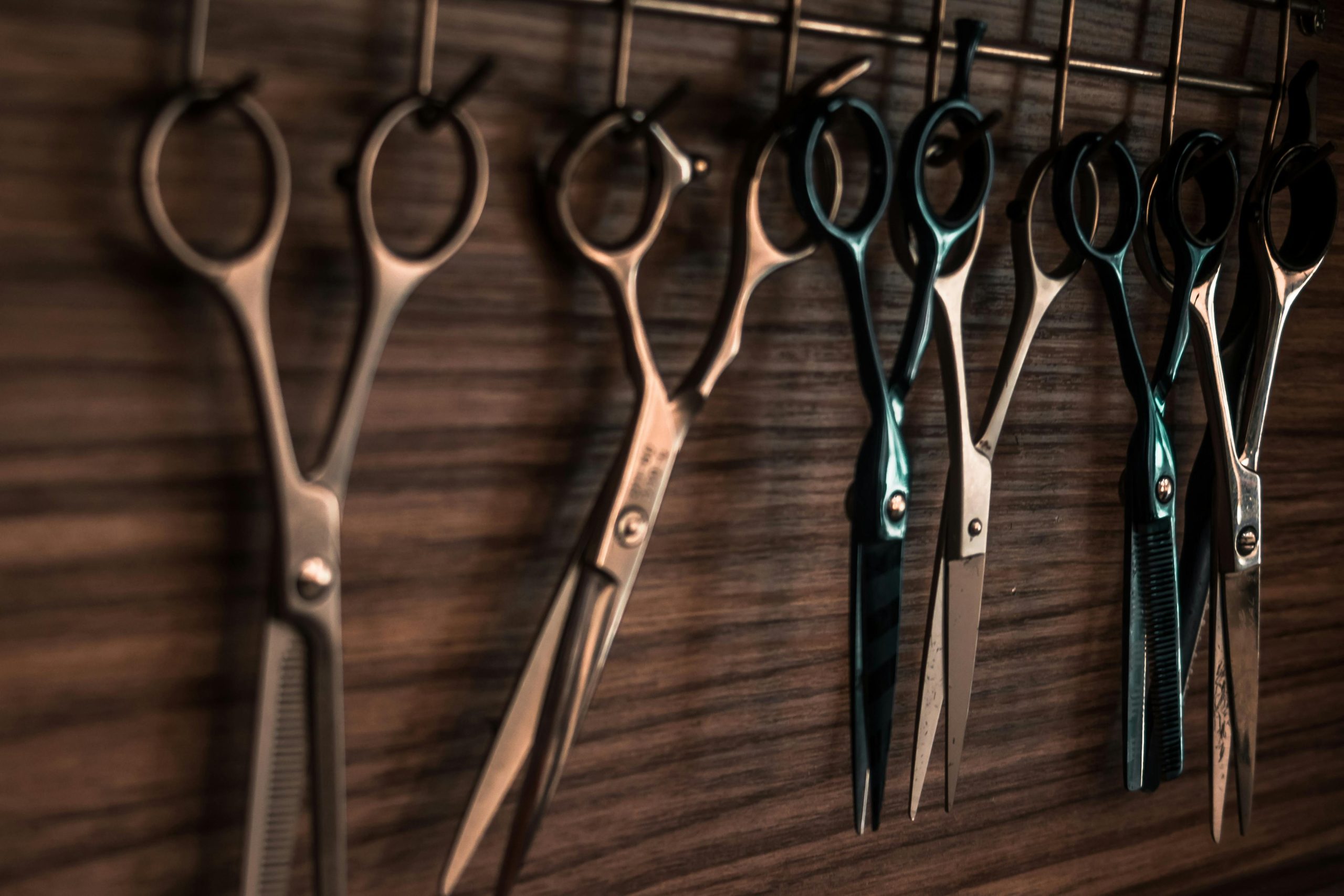 A collection of vintage barber scissors hanging on a wooden wall, showcasing sharp tools for hair cutting.