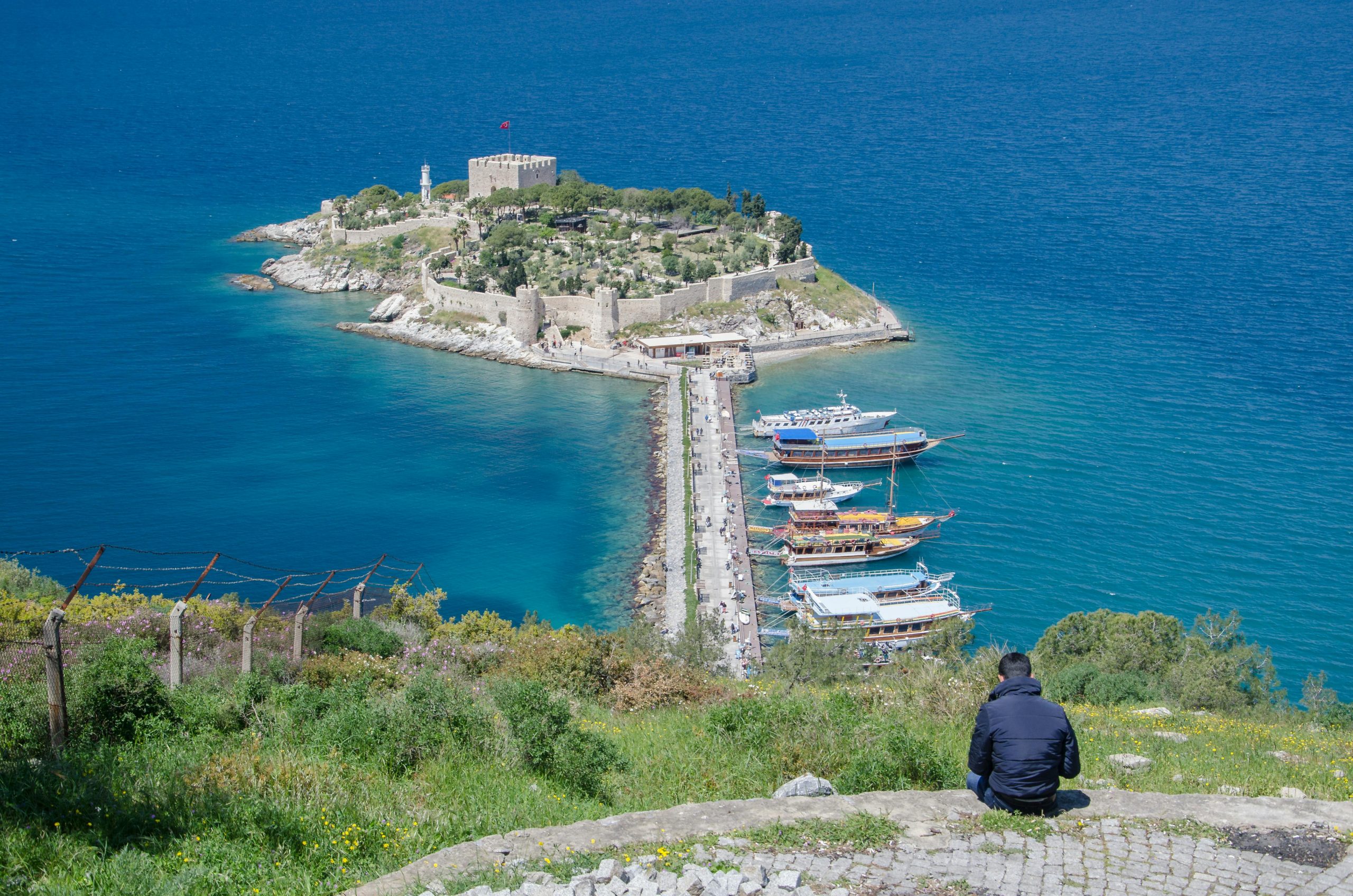 Aerial view of Güvercinada Island and boats in Kuşadası, Turkey, with a person sitting and enjoying the scenery.