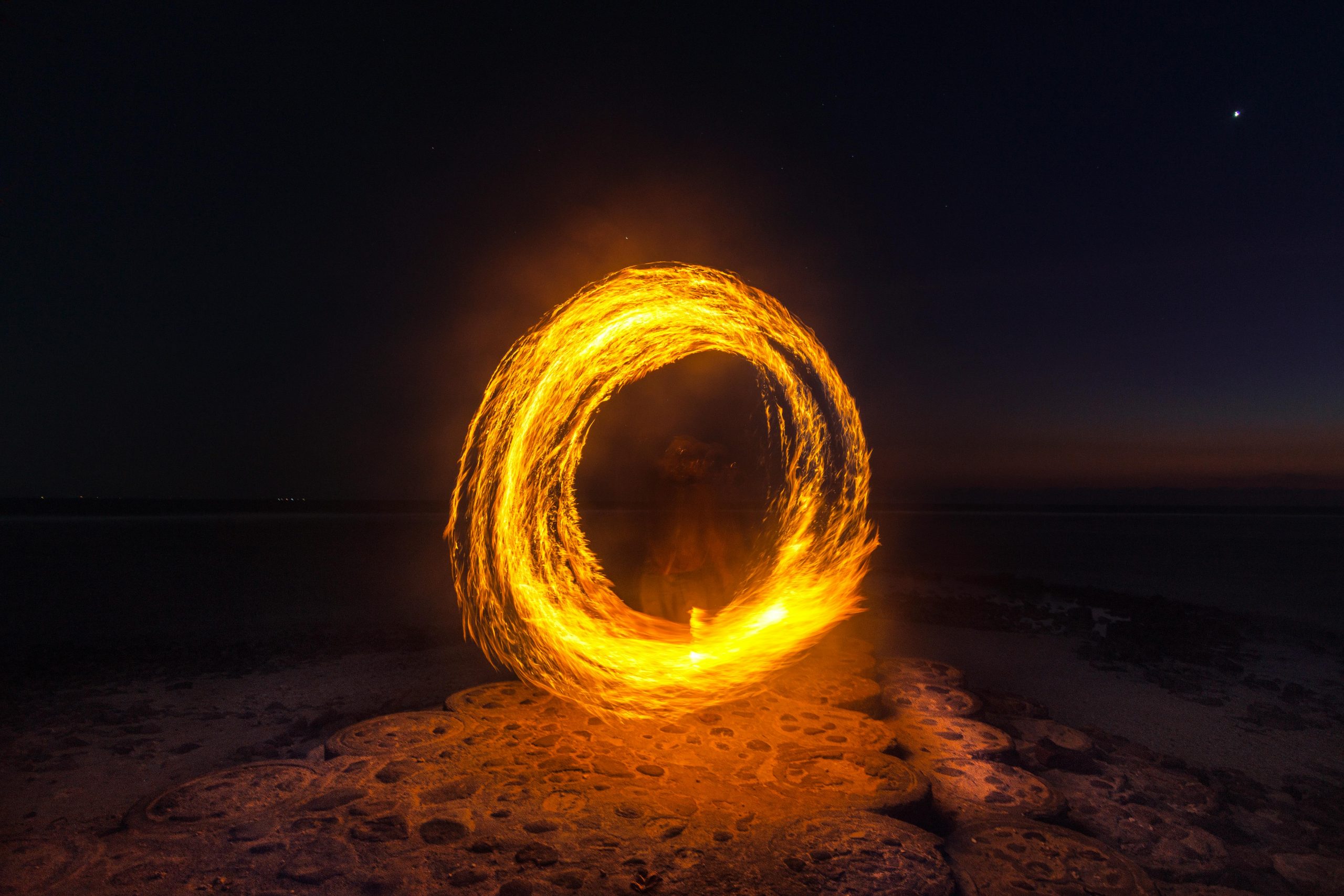 Captivating long exposure shot of a fire dancer creating fiery circles on a serene beach at night.