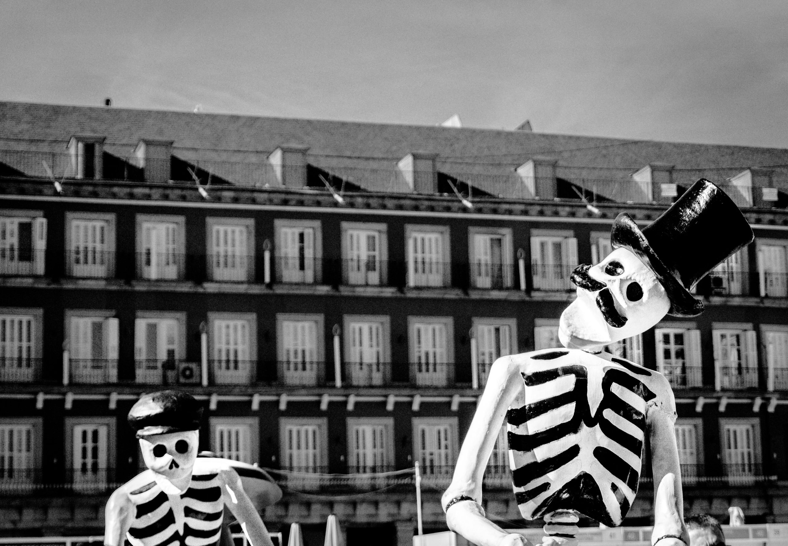 Black and white photo of skeletons with top hats outside a building.