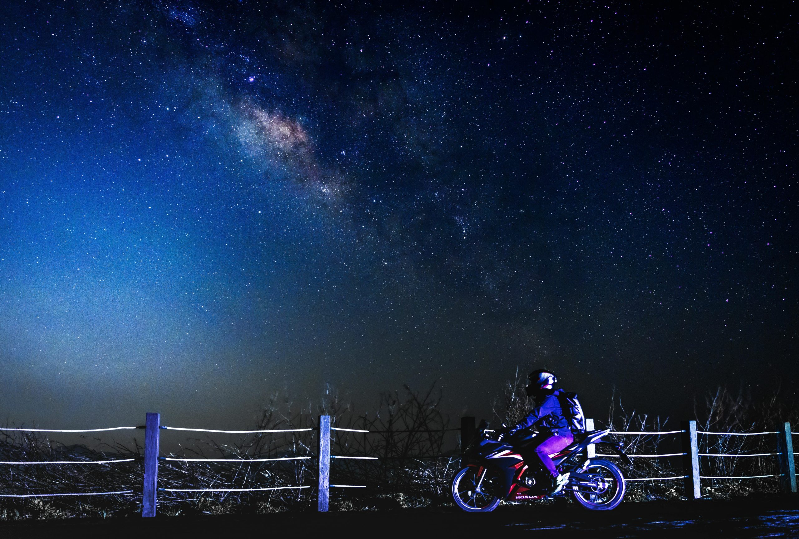 A motorcyclist rides under a stunning starry galaxy, showcasing the breathtaking night sky beauty.