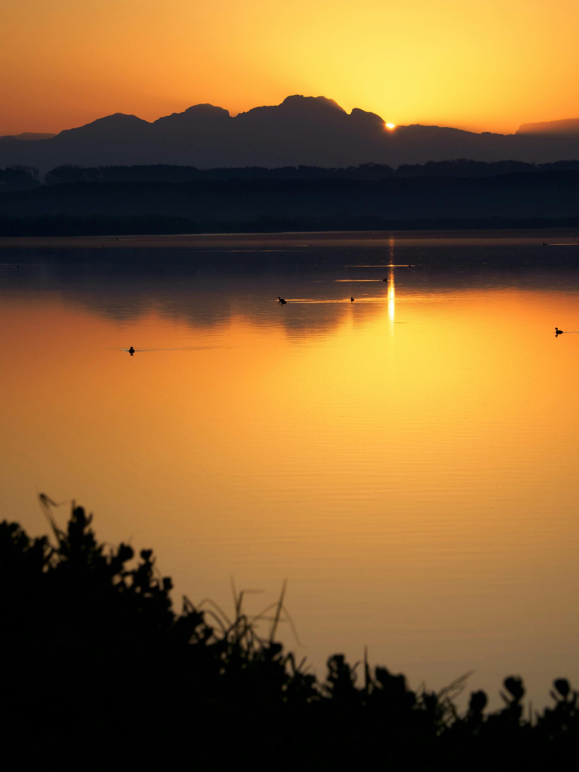 Stunning sunset reflecting over a calm lake in Cape Town, South Africa, with silhouetted mountains.