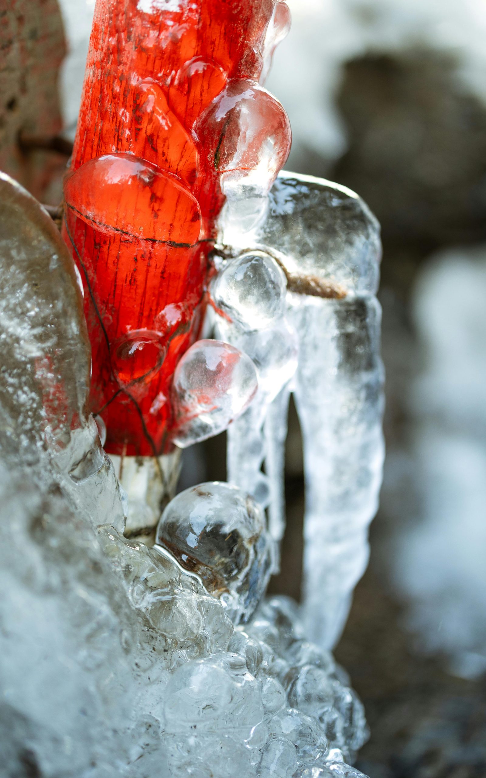 Detailed view of ice formations on a red pipe, highlighting winter's freezing beauty.