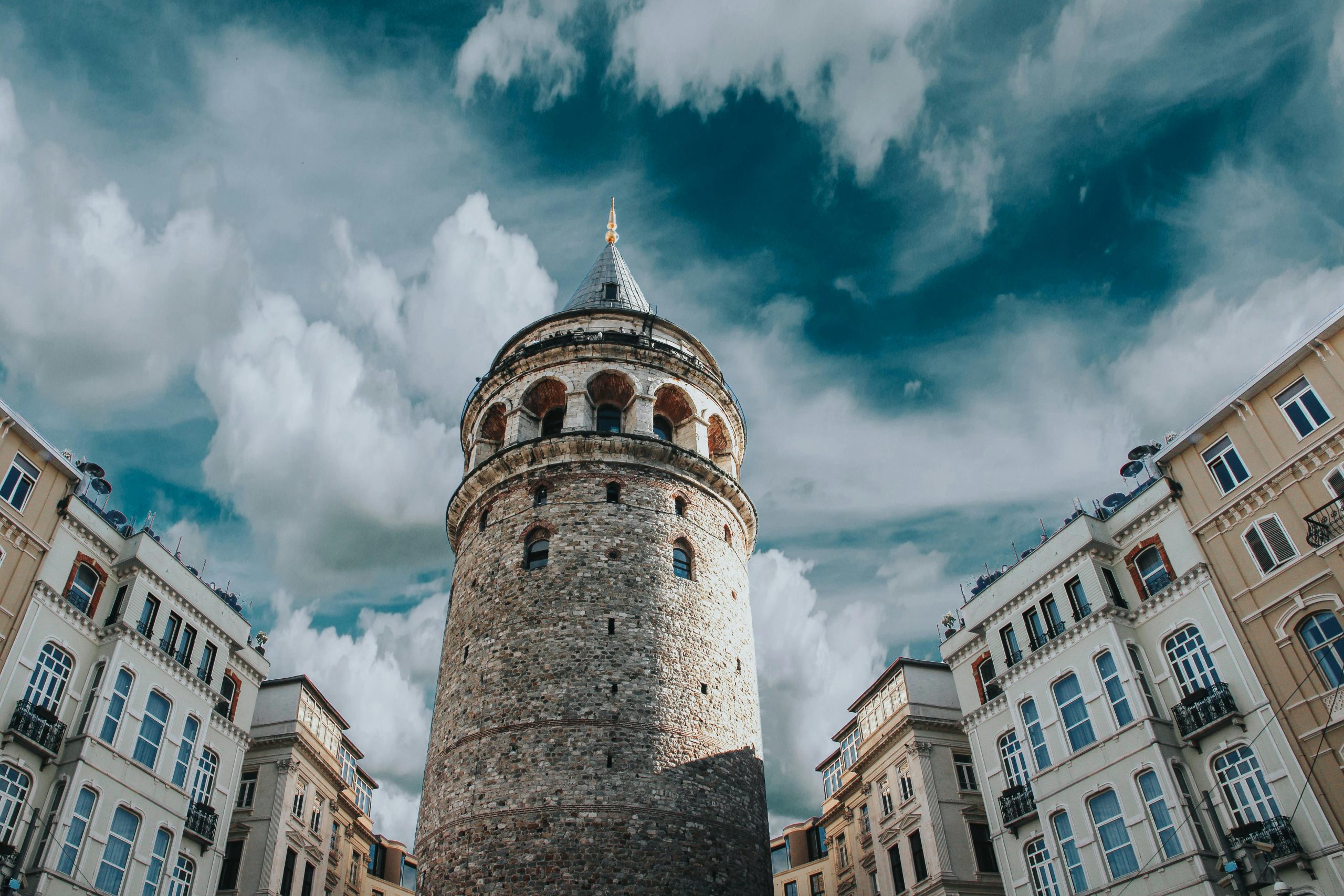 Captivating view of Galata Tower surrounded by historic architecture and dramatic clouds in Istanbul, Turkey.