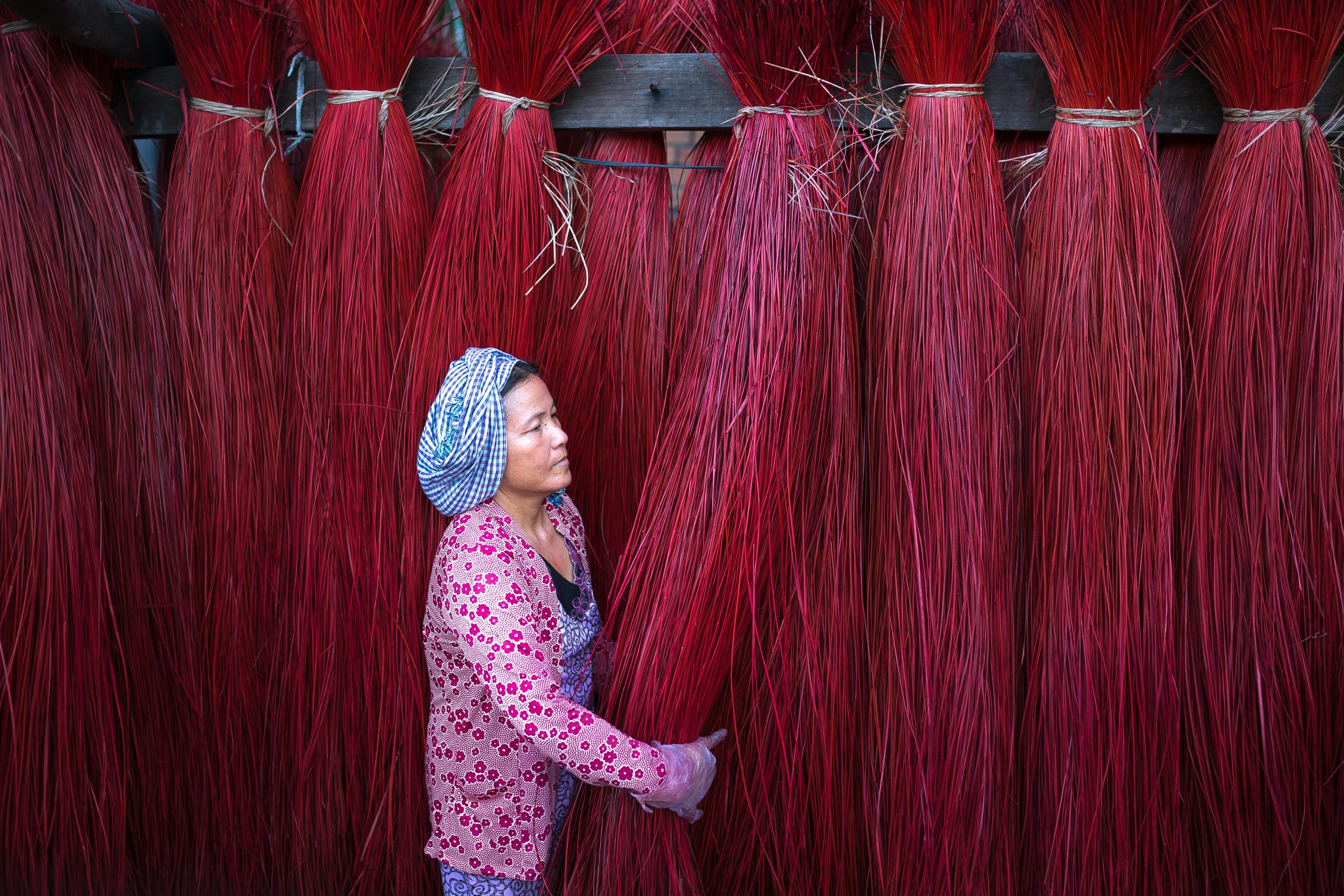 A woman in traditional attire handles vibrant red fibers, showcasing cultural craftsmanship.