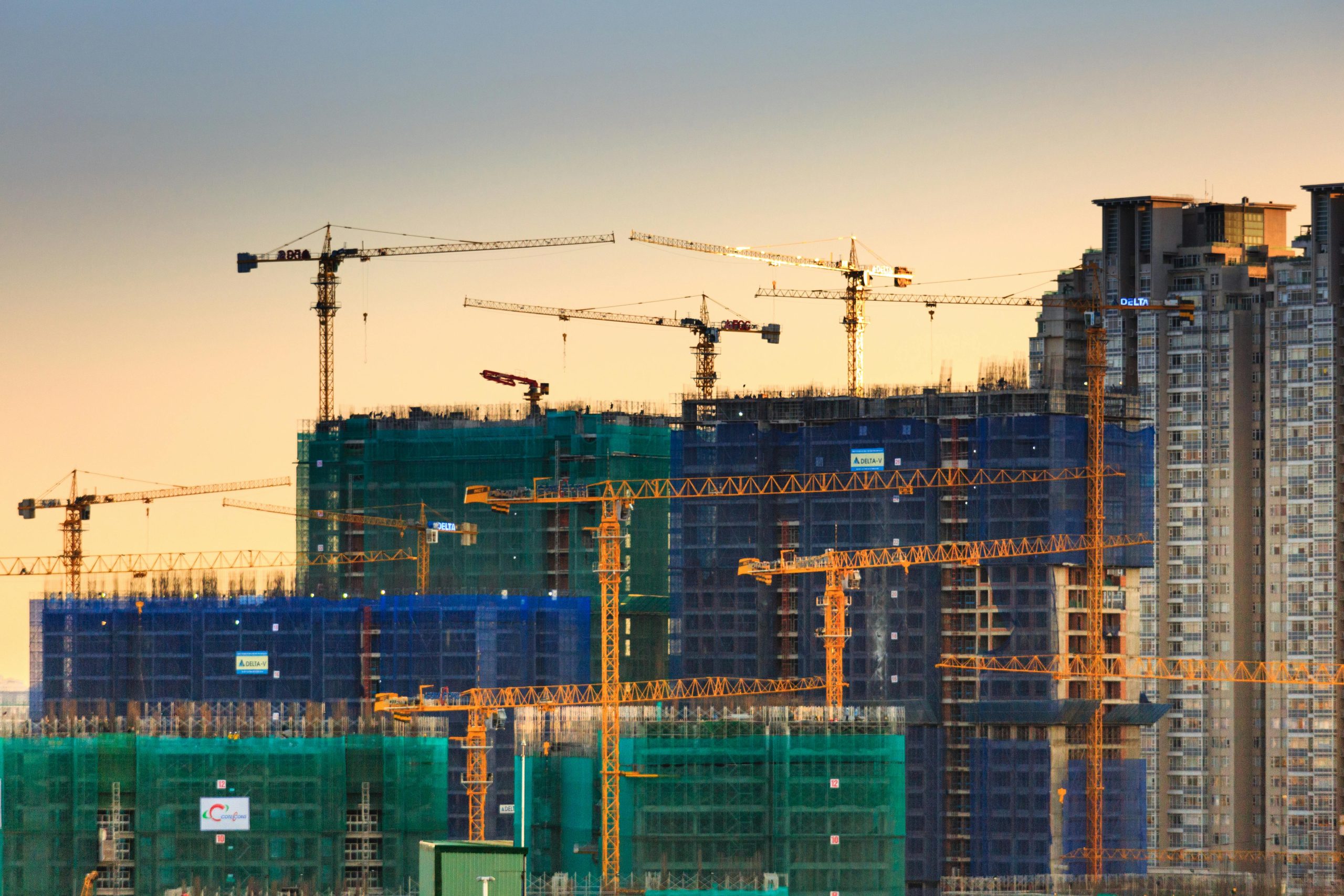 A cityscape featuring high-rise buildings under construction with cranes during sunset.