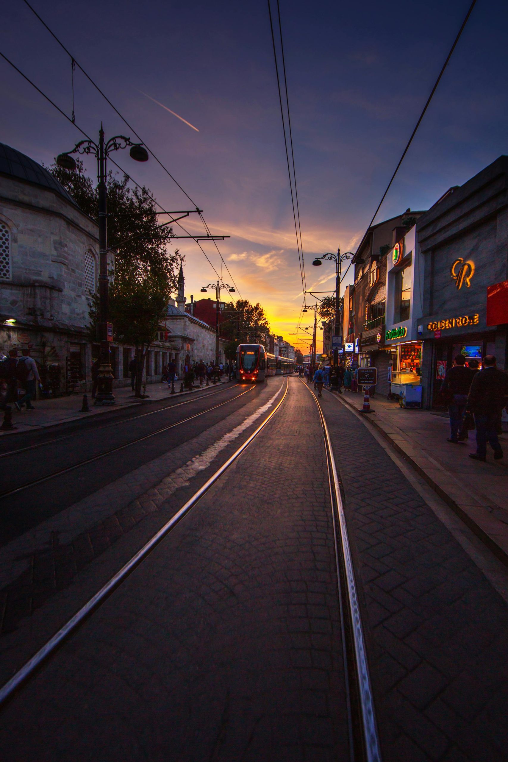 Vibrant sunset over Istanbul street with tram lines and bustling evening activity.