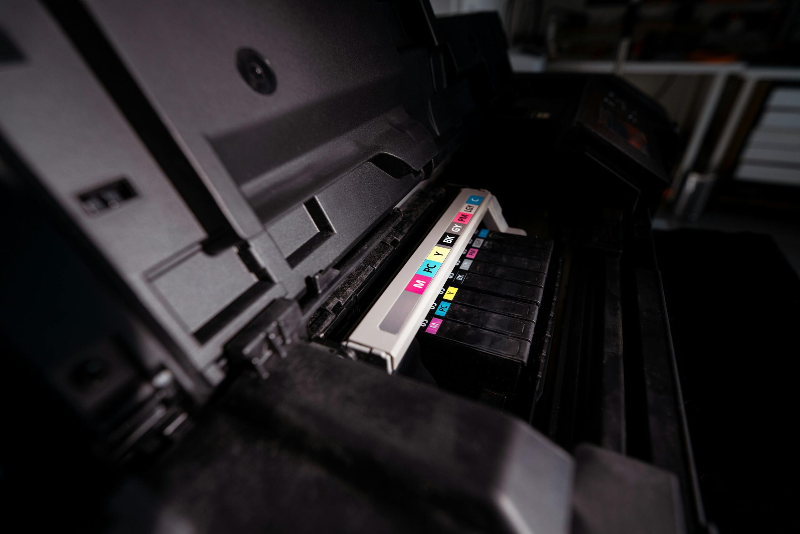 Detailed view of open printer with visible CMYK ink cartridges in a dark setting.