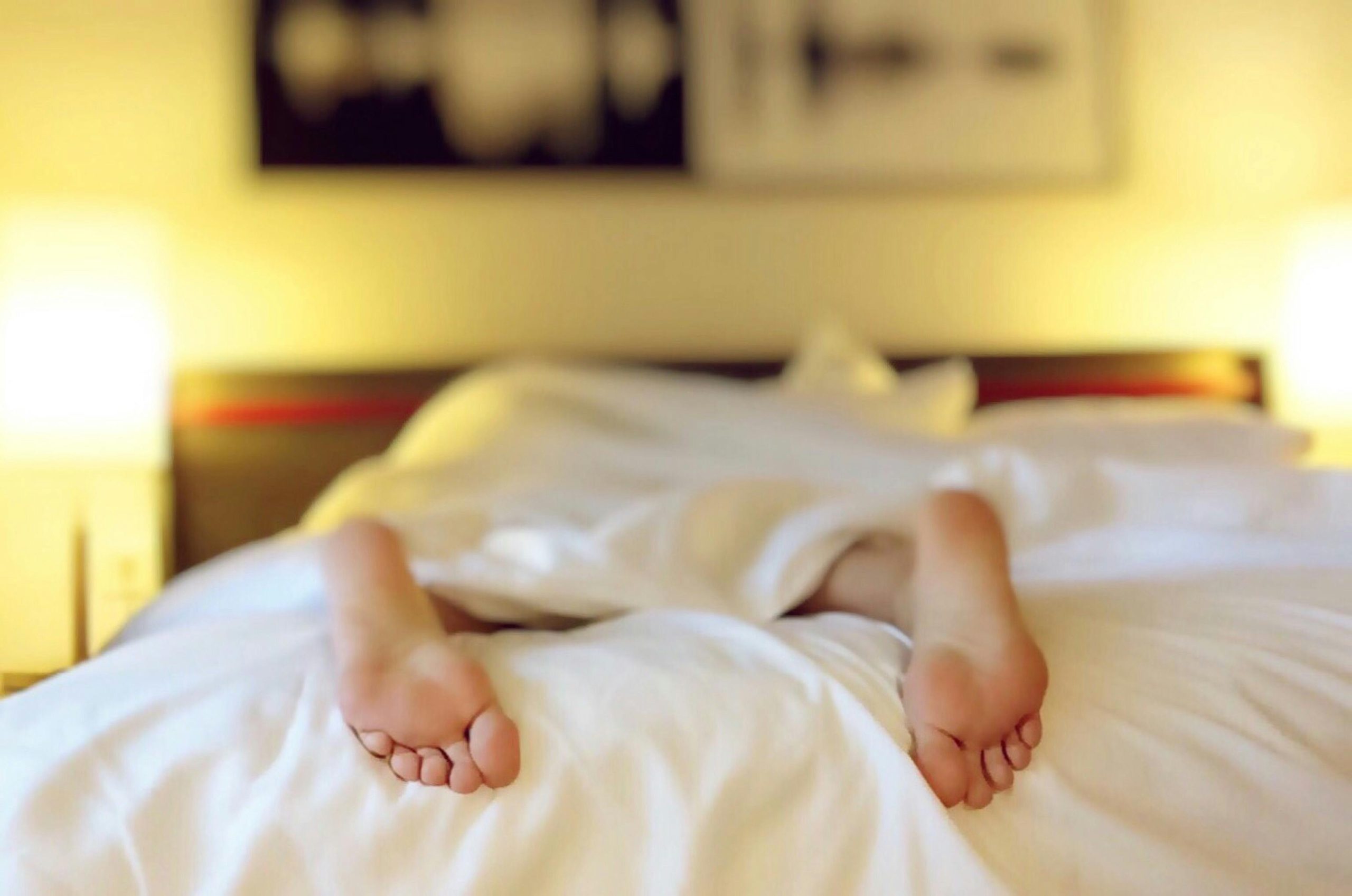 A person relaxing on a bed with feet under white sheets, conveying serenity.