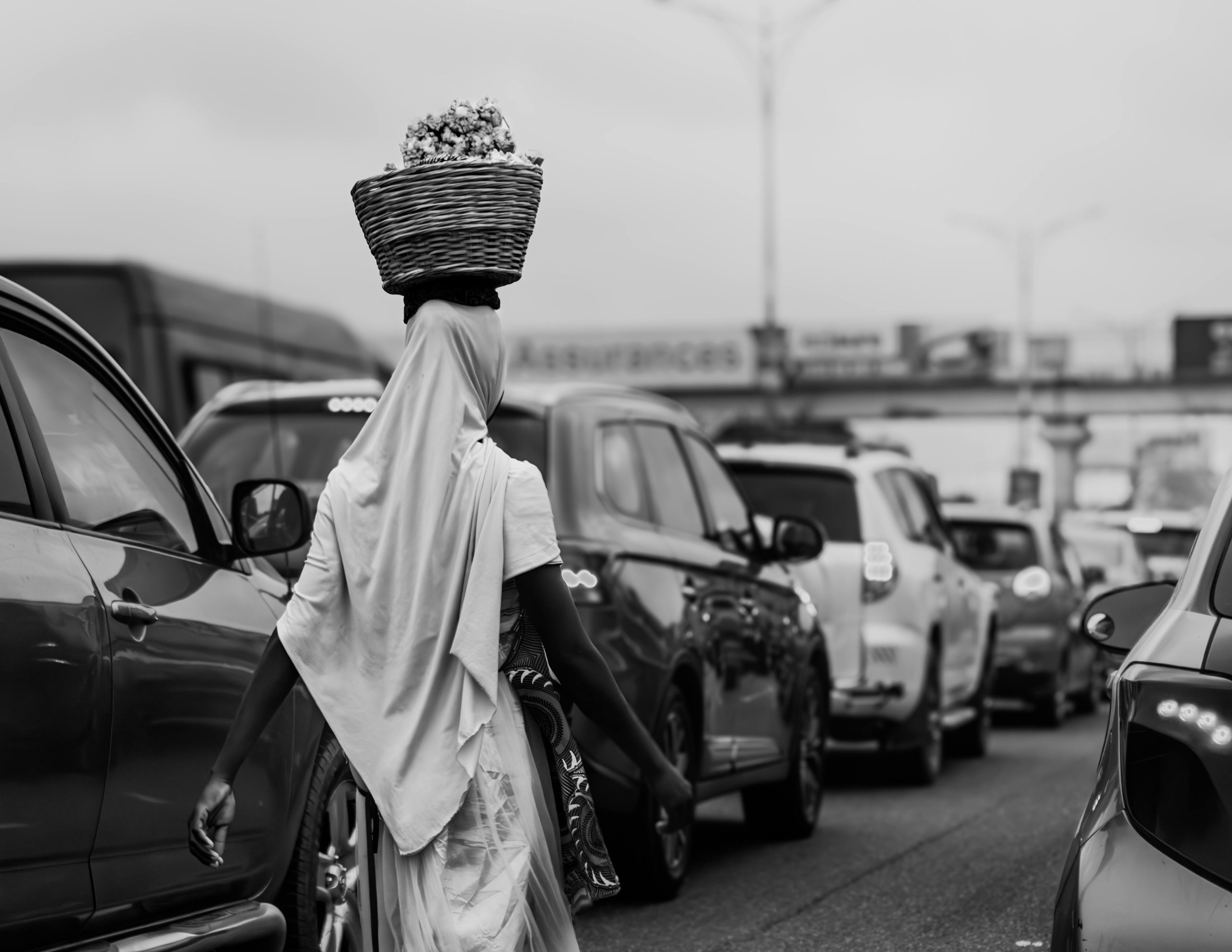 Black and white photo of a woman vendor in Accra carrying a basket.