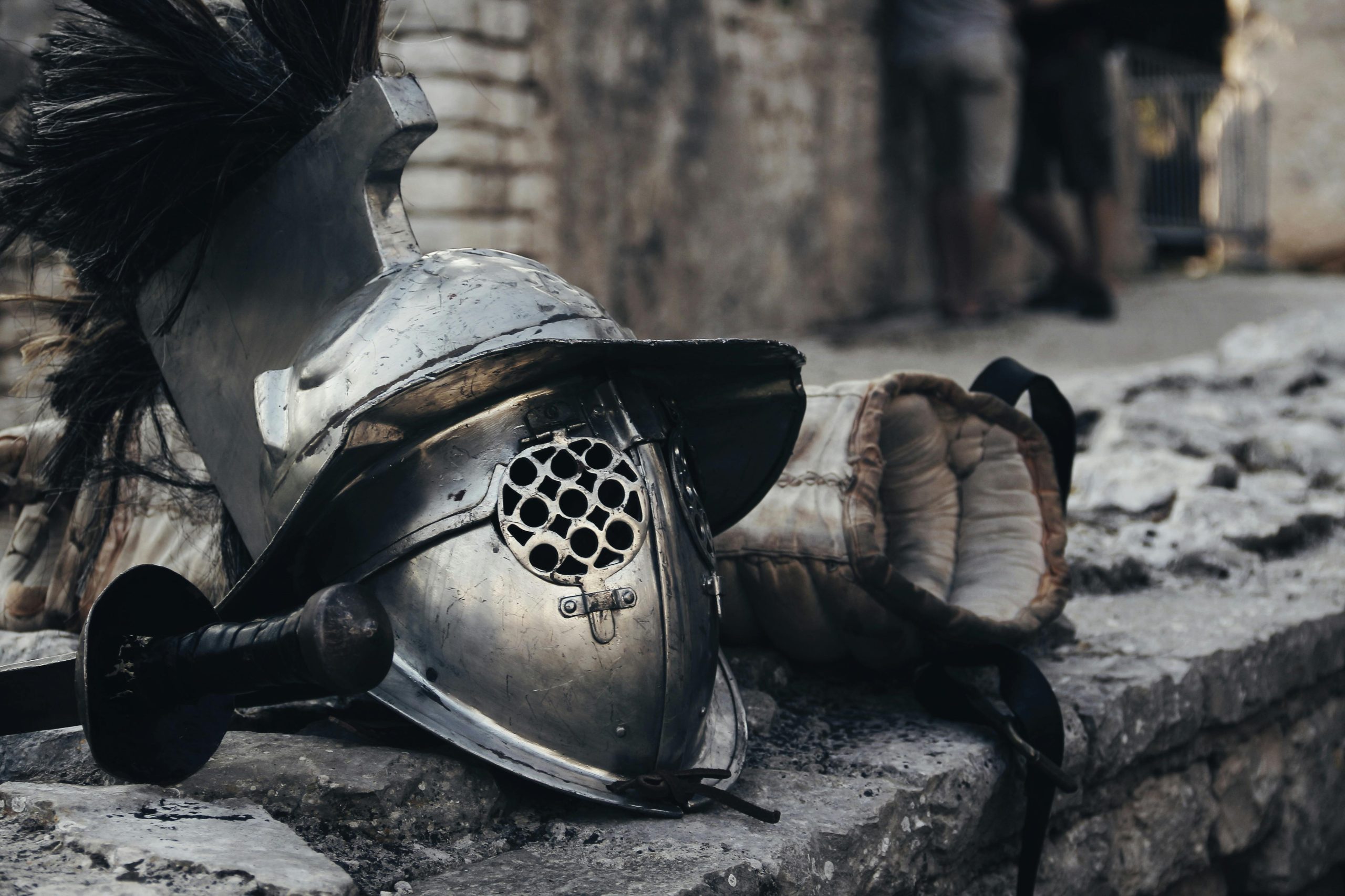 A medieval armor helmet, sword, and glove against a stone wall depicting historical combat gear.