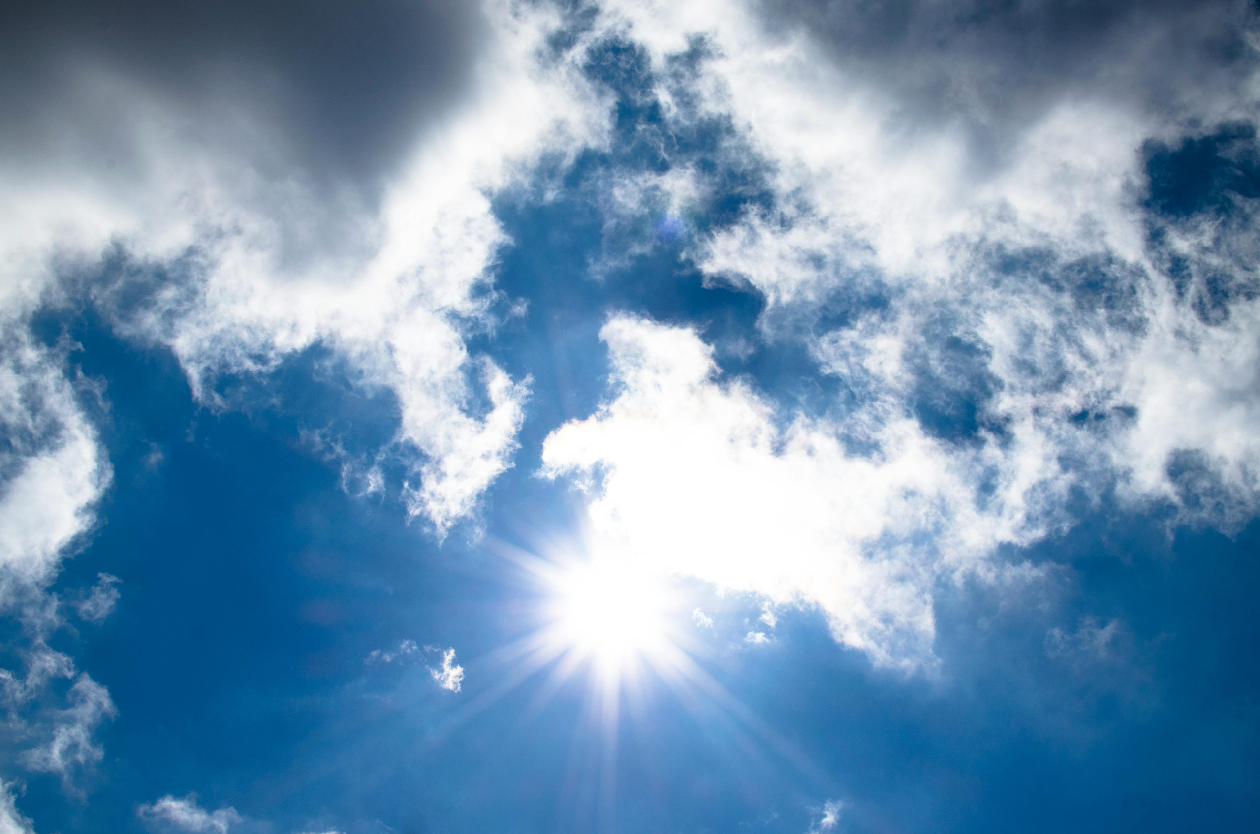 A vivid view of the sun shining through fluffy clouds in a bright blue sky.