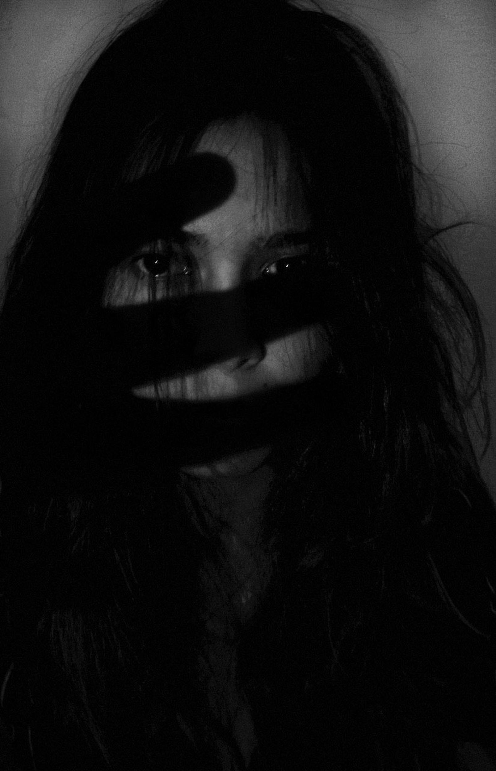 A dramatic black and white portrait of a woman with shadows cast across her face, creating a mysterious and eerie mood.