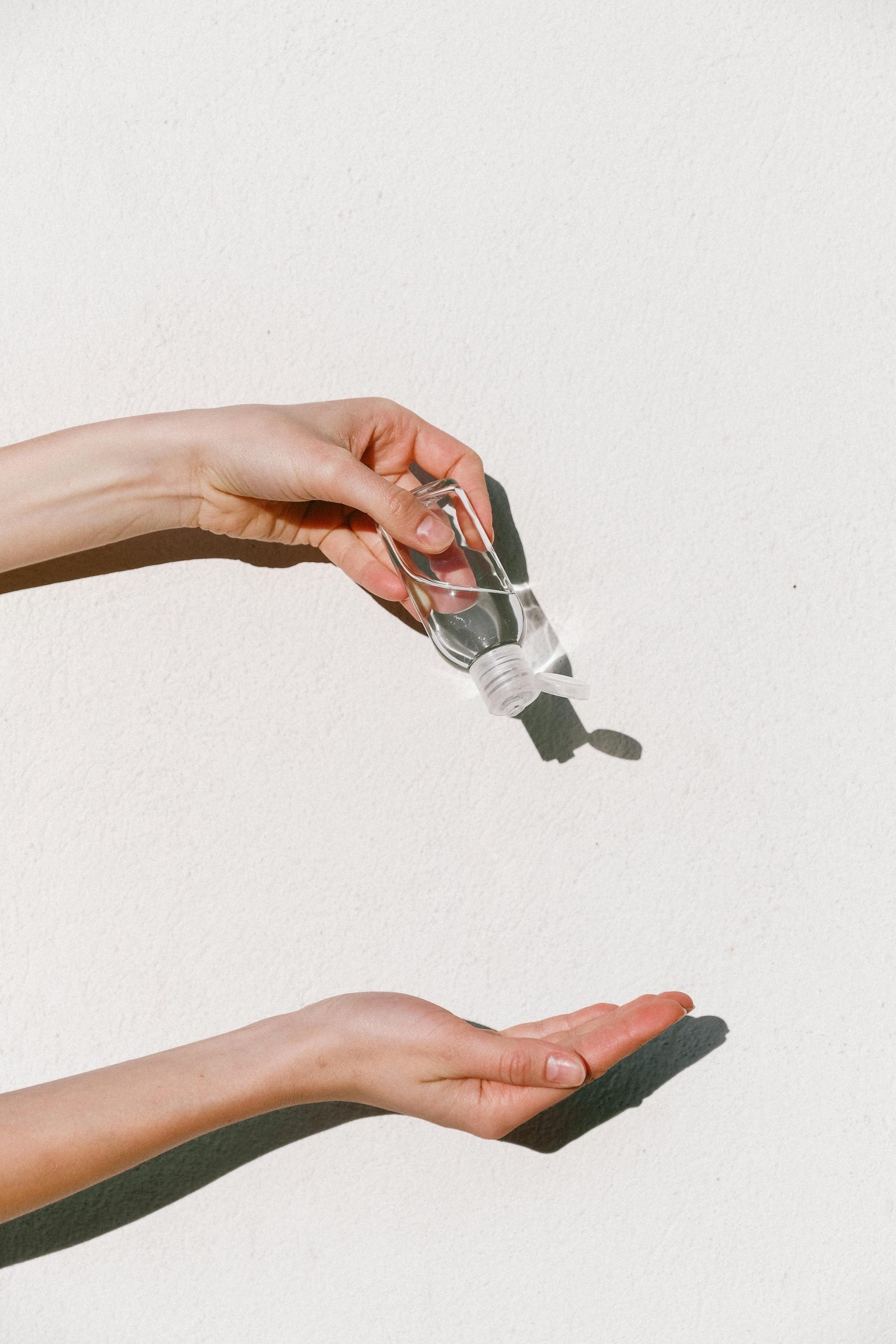 Person applying hand sanitizer against white backdrop, emphasizing hygiene and protection.