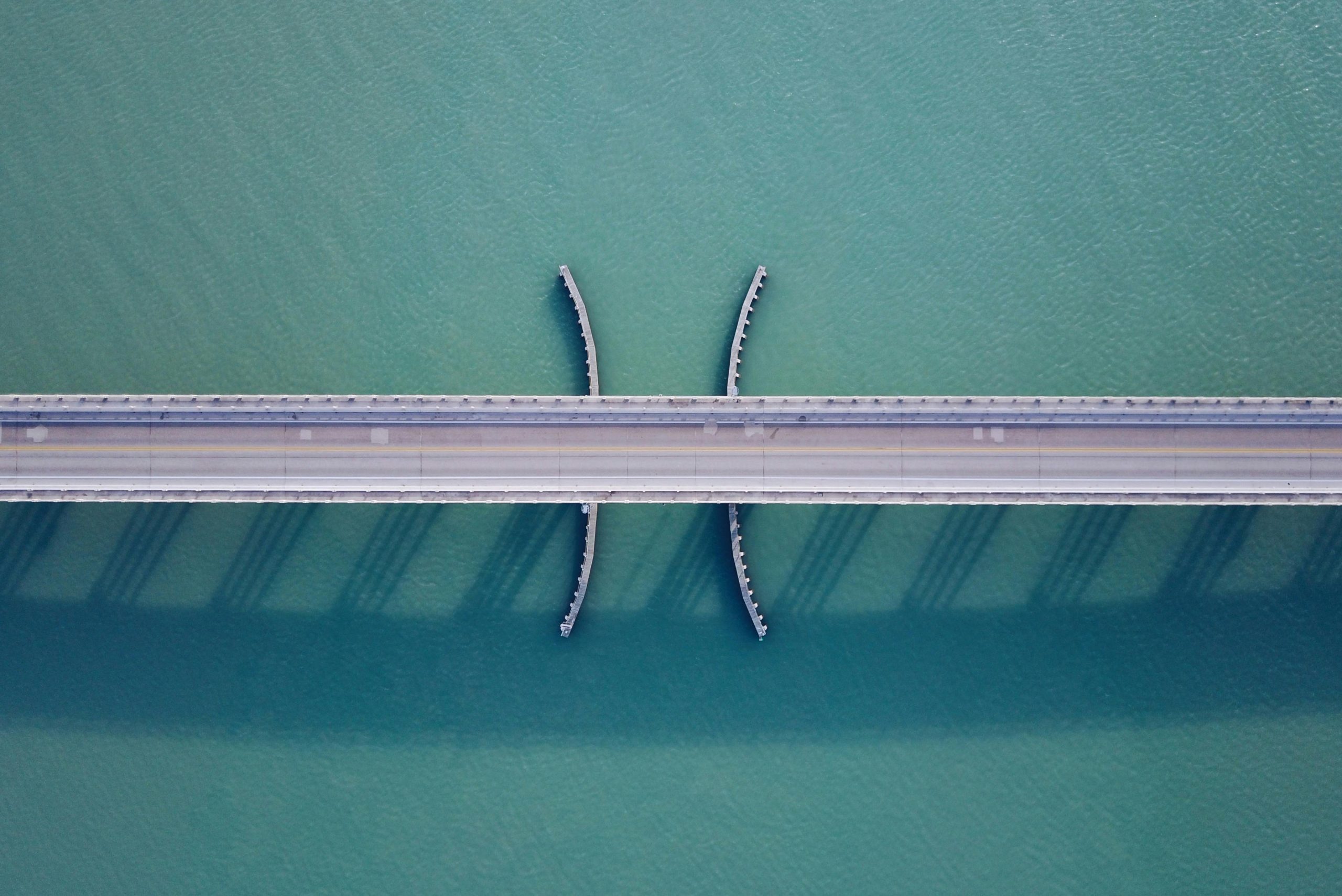 Aerial shot of a bridge over clear blue water, showcasing modern architecture and symmetry.