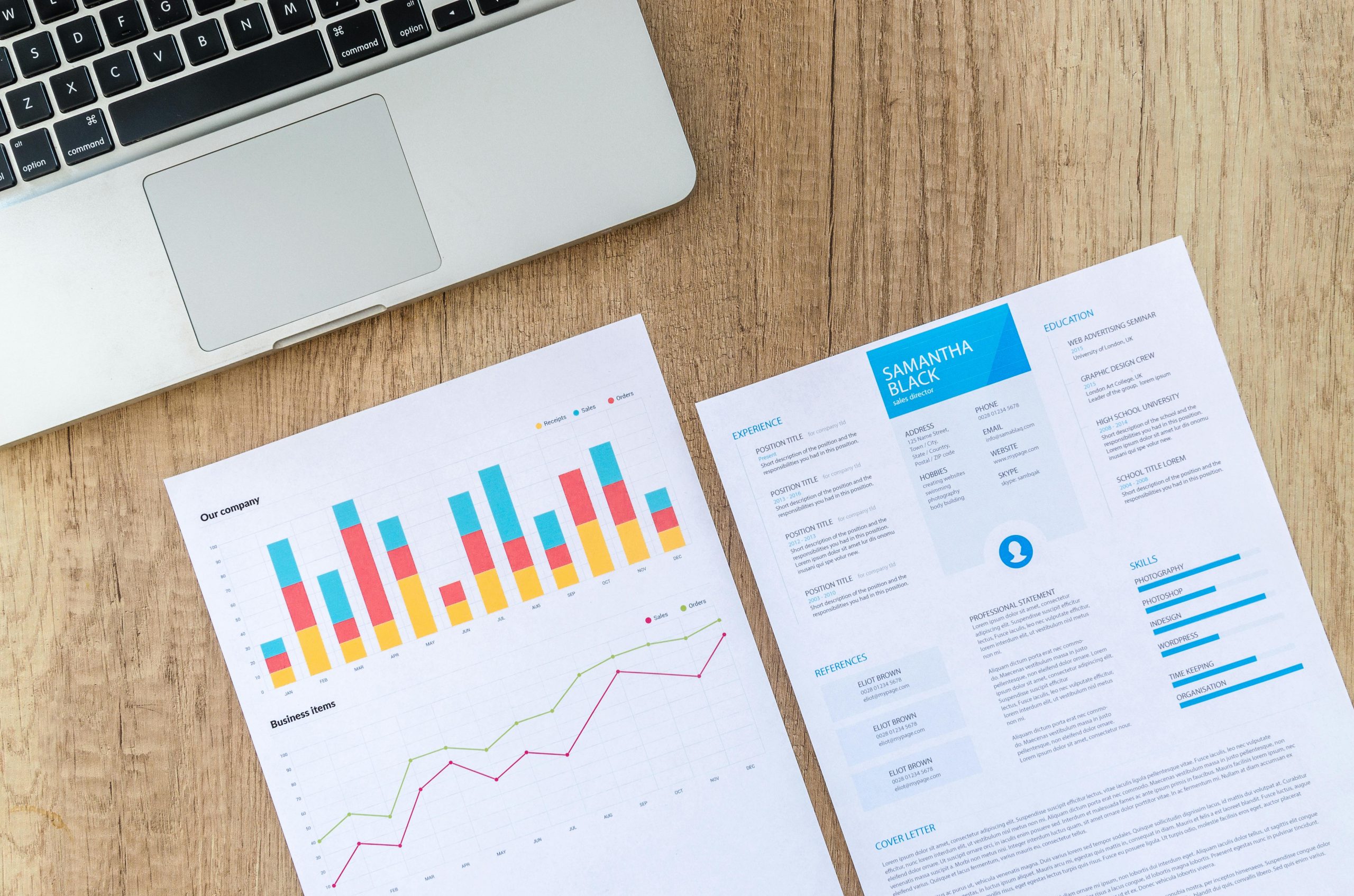 Top view of a laptop, charts, and resume on a wooden desk, showcasing business analysis and job application.