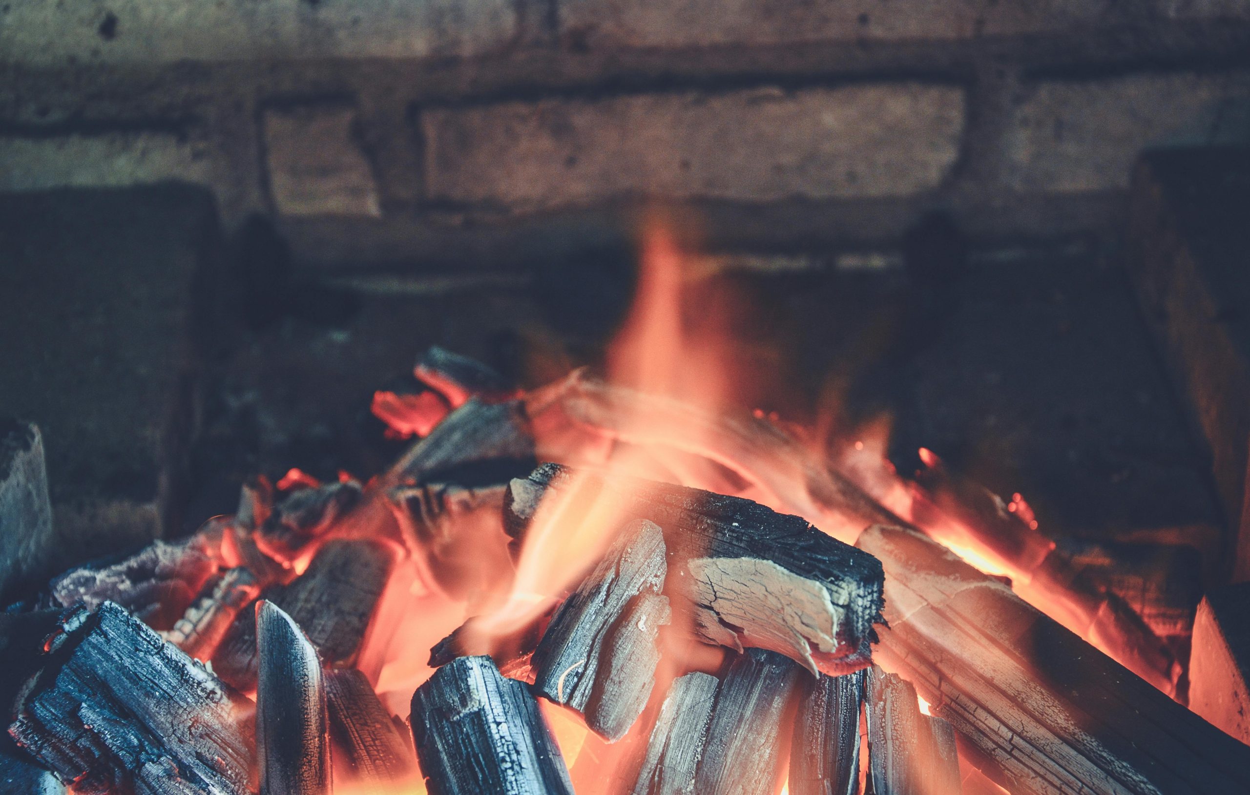 Warm glowing embers and flames from firewood in a rustic fireplace setting.