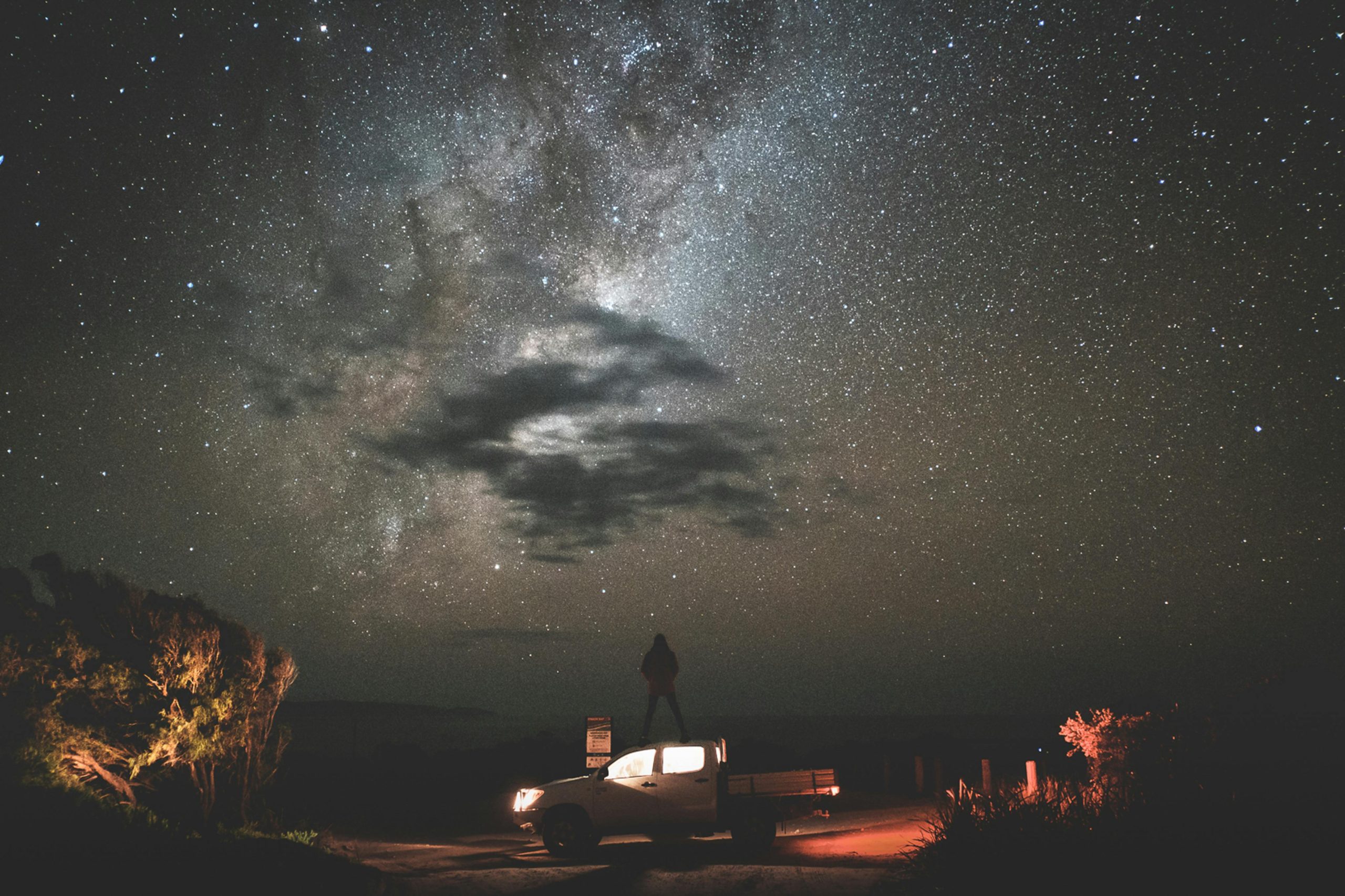 A silhouette on a car under a stunning starry sky and Milky Way, capturing the essence of night adventure.
