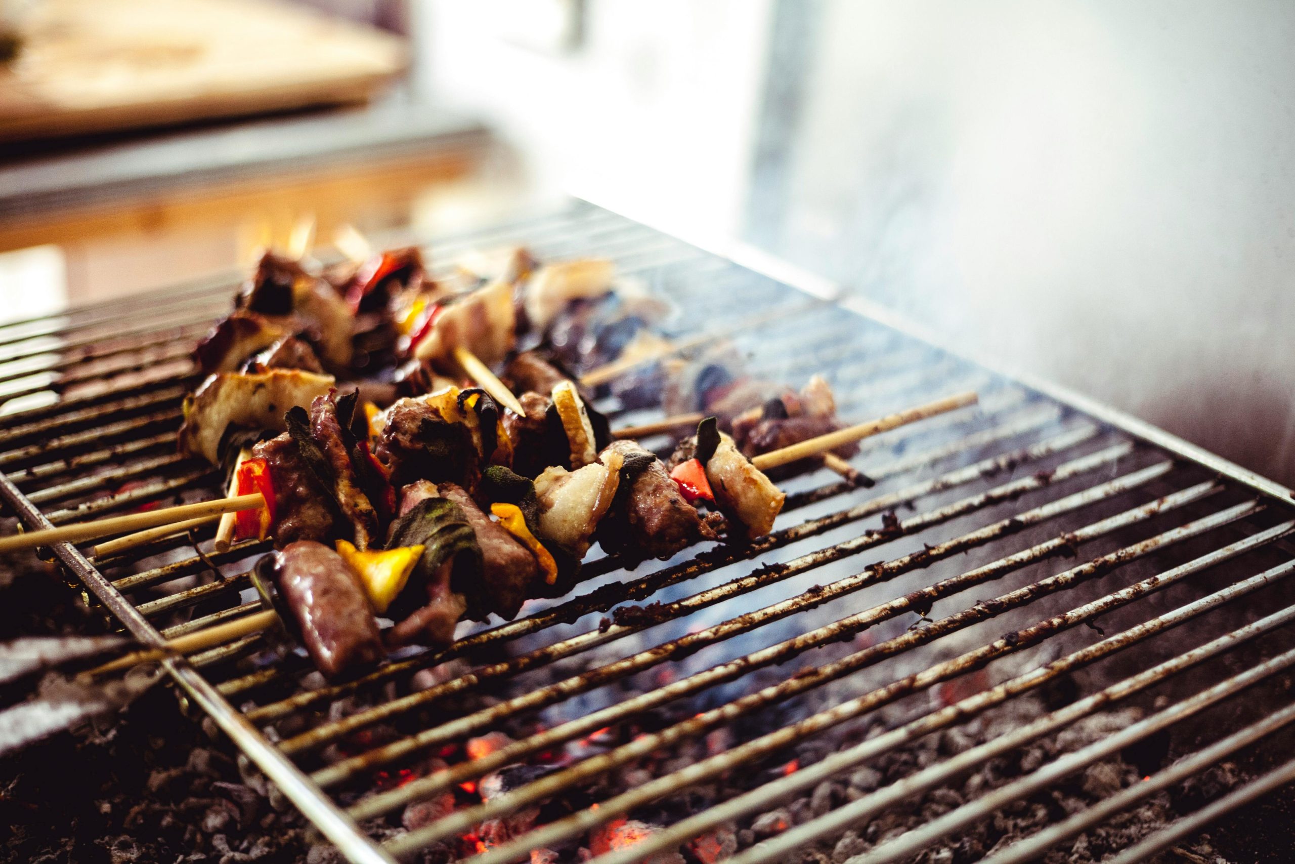 Close-up of delicious skewers grilling over hot charcoal with smoke rising.