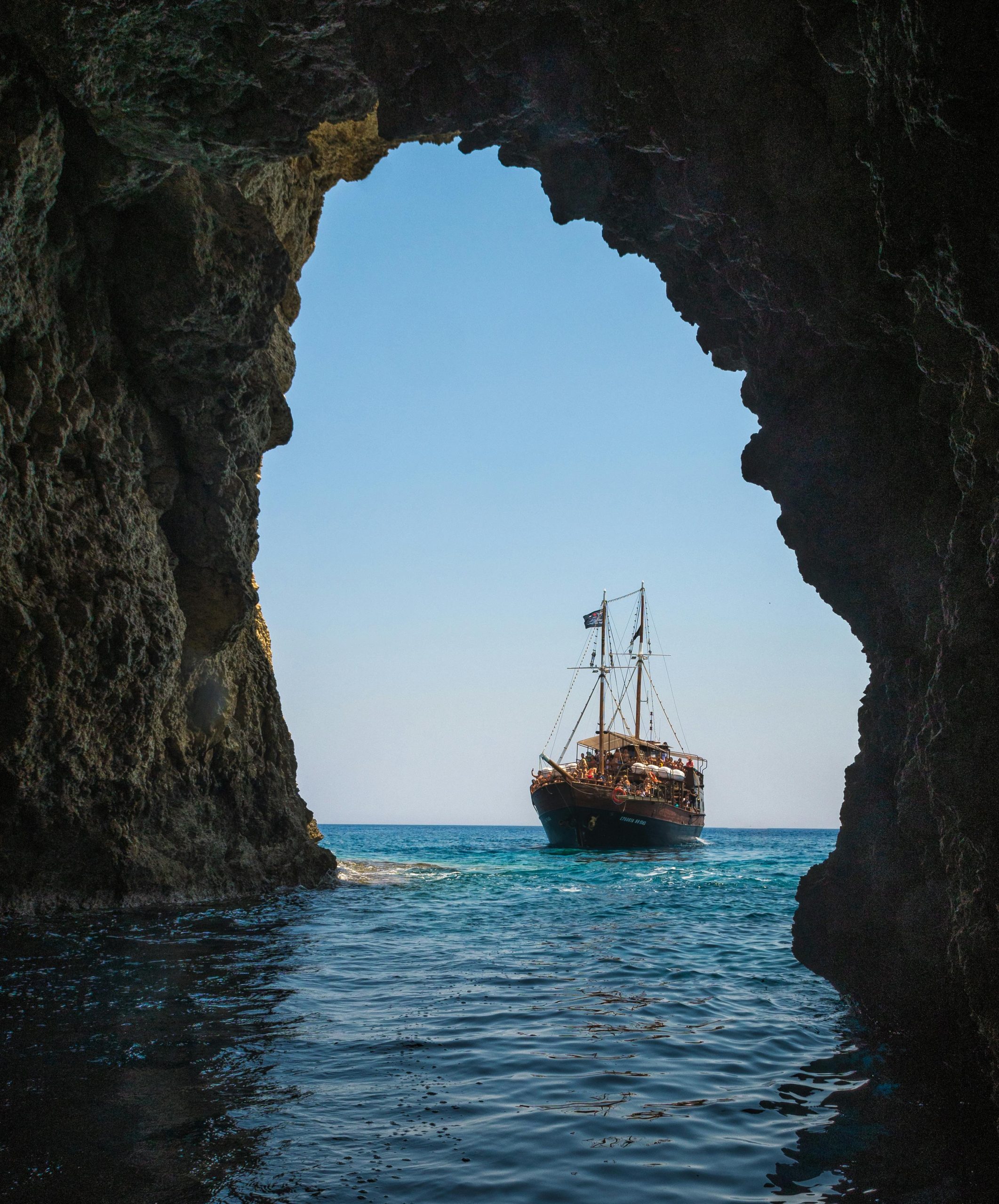 A stunning view of a ship sailing through a rocky sea cave in Rethymno, Greece.