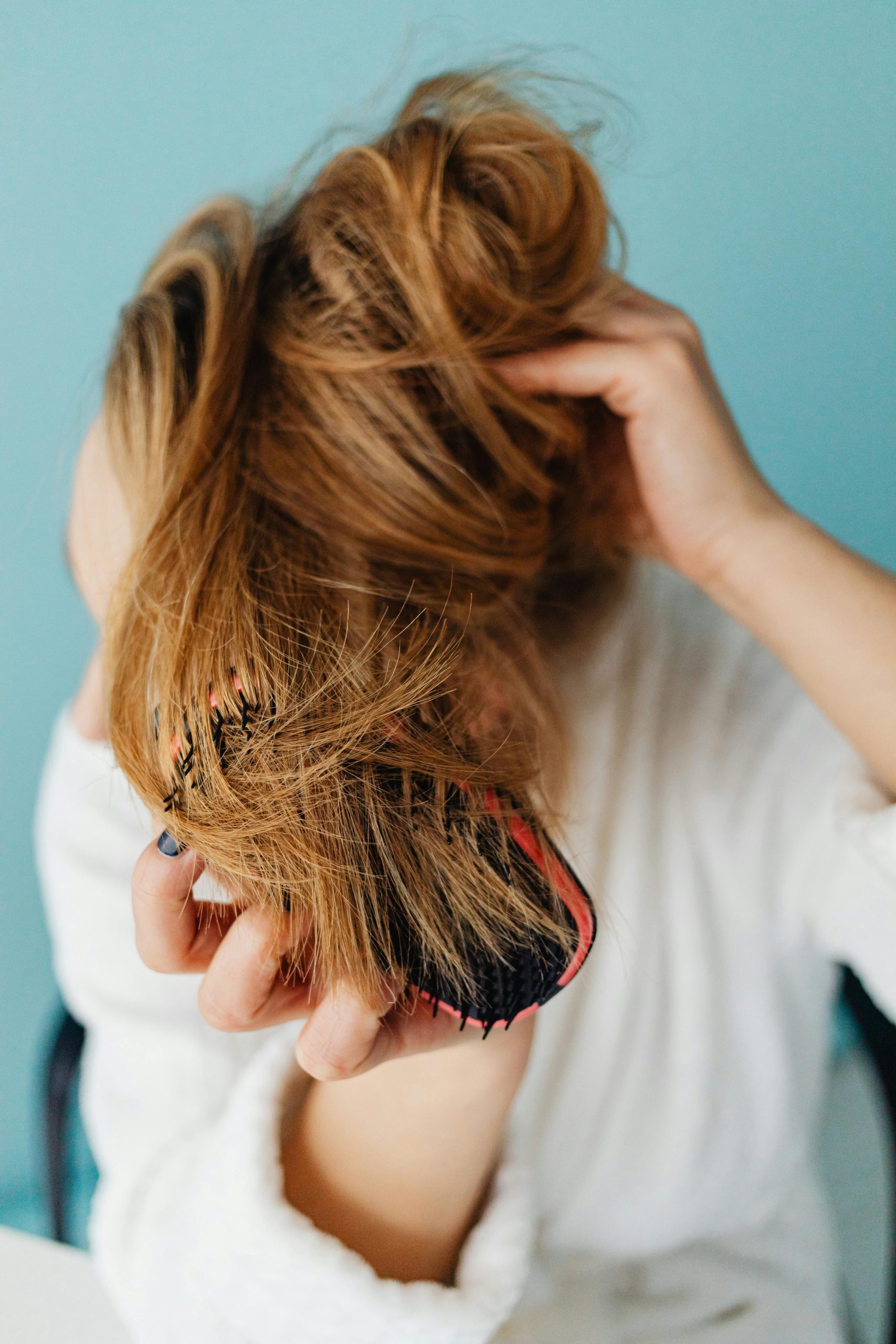 Close-up of a woman brushing her blonde hair in a casual setting.