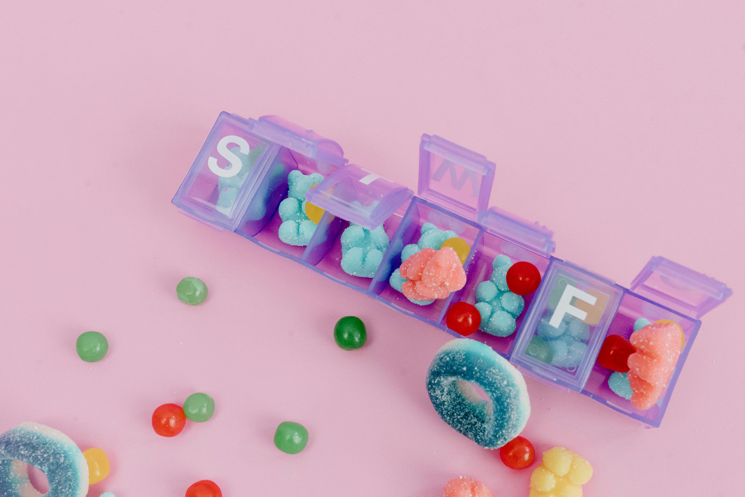 Vibrant gummy candies arranged in a pill organizer on a pink background.