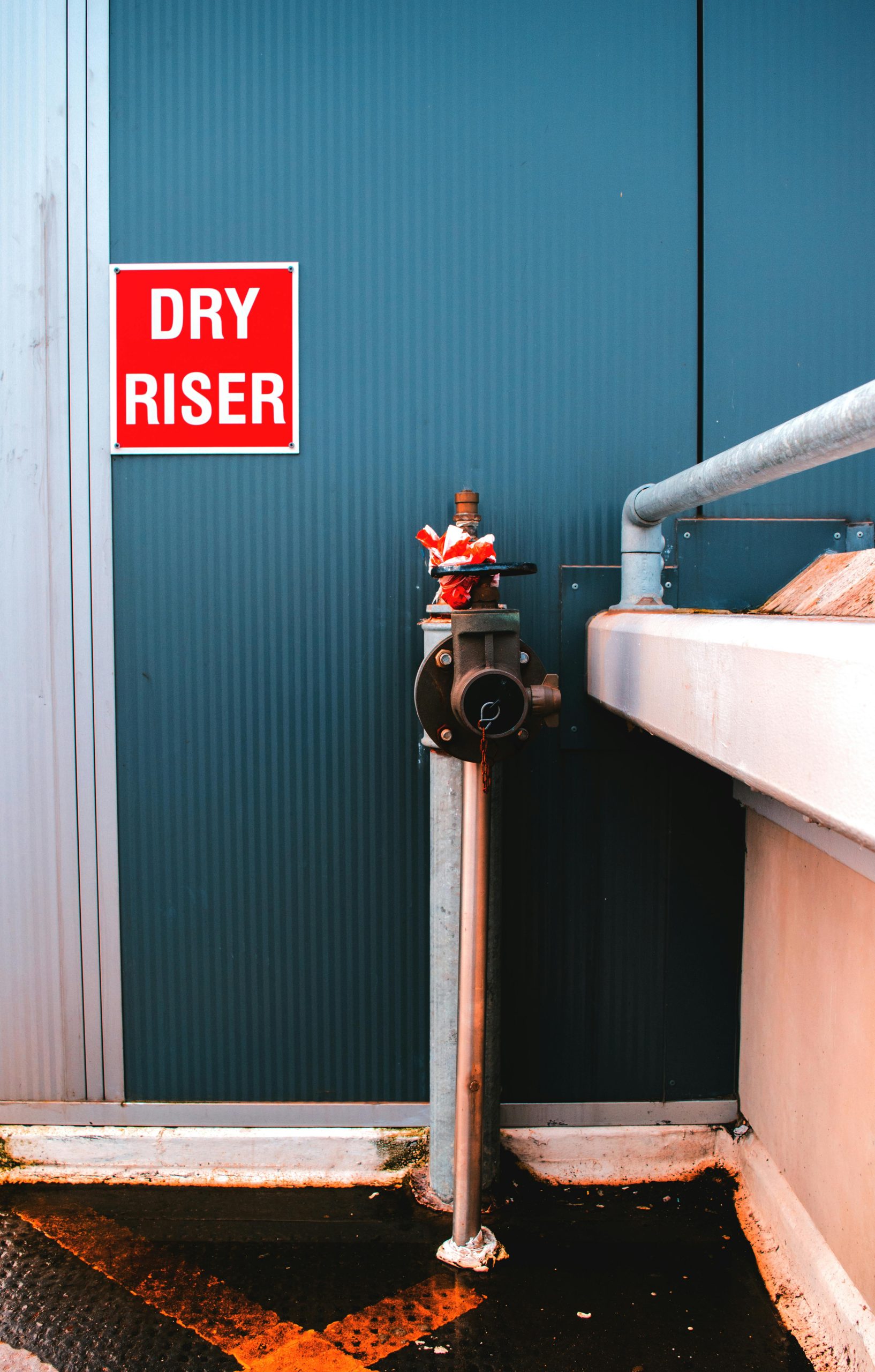 A modern dry riser system and steel pipes against a blue wall in an urban setting.