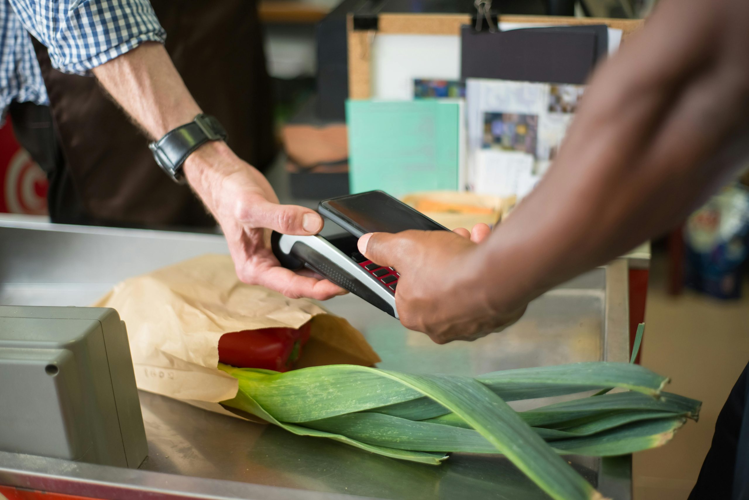 A customer making a contactless payment with a smartphone at a grocery store checkout counter.