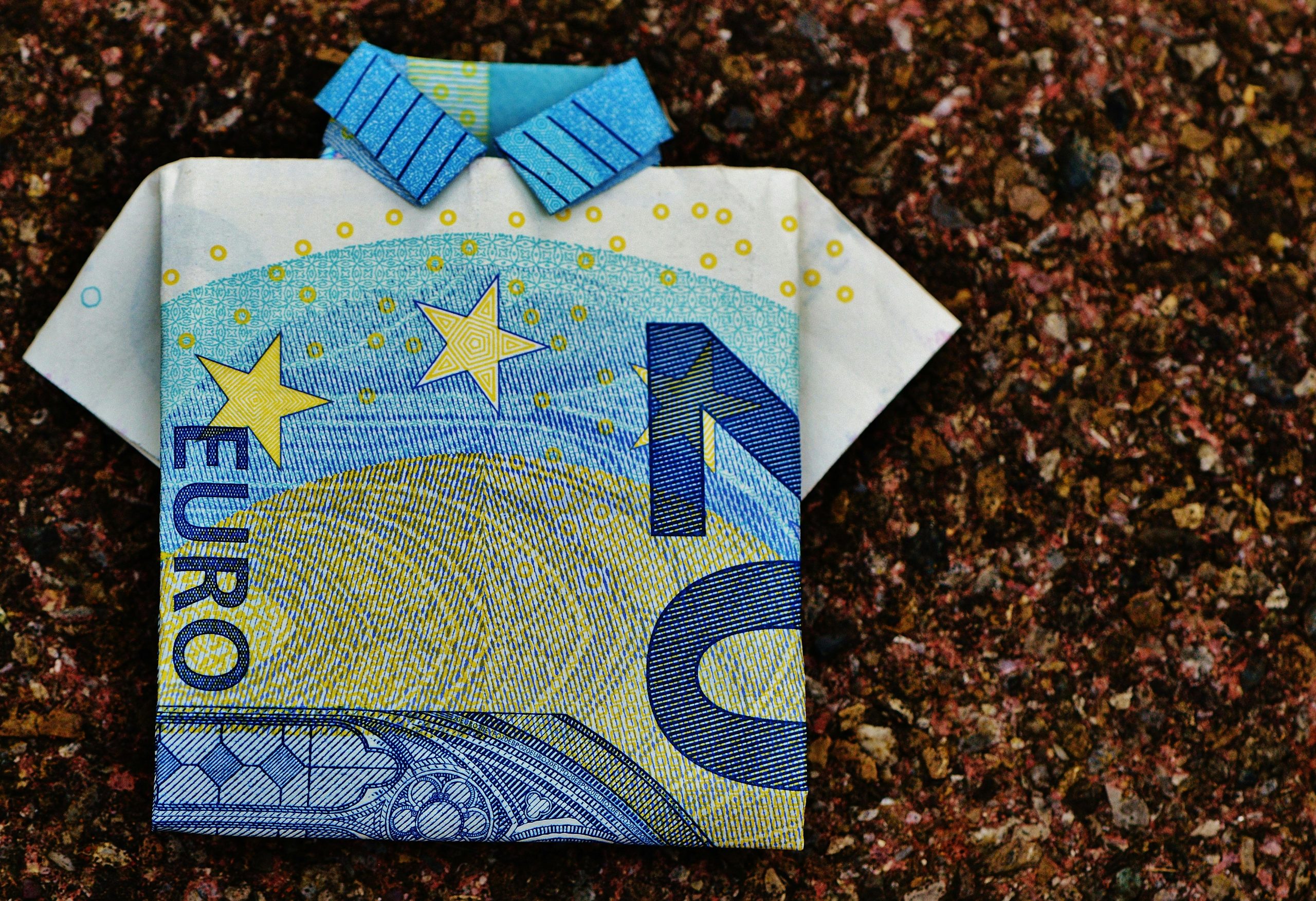 A 10 euro banknote folded into an origami shirt on a textured background showcasing creativity.